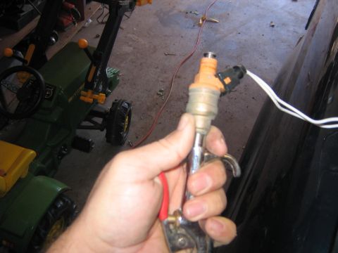 1994 Ford Bronco - A fuel injector is held in a hand, with wires connected to its top.