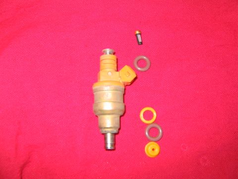 1994 Ford Bronco - A single fuel injector and its associated O-rings are laid out on a red surface.