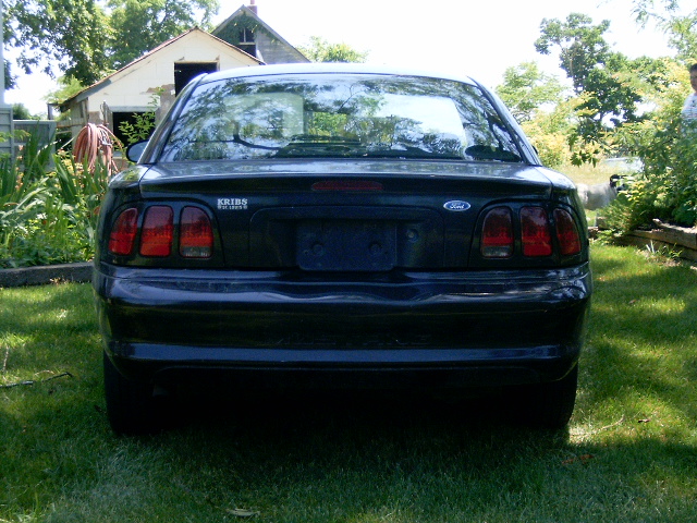 Dark Ford Mustang rear view, showing taillights and Ford emblem. License plate area is empty