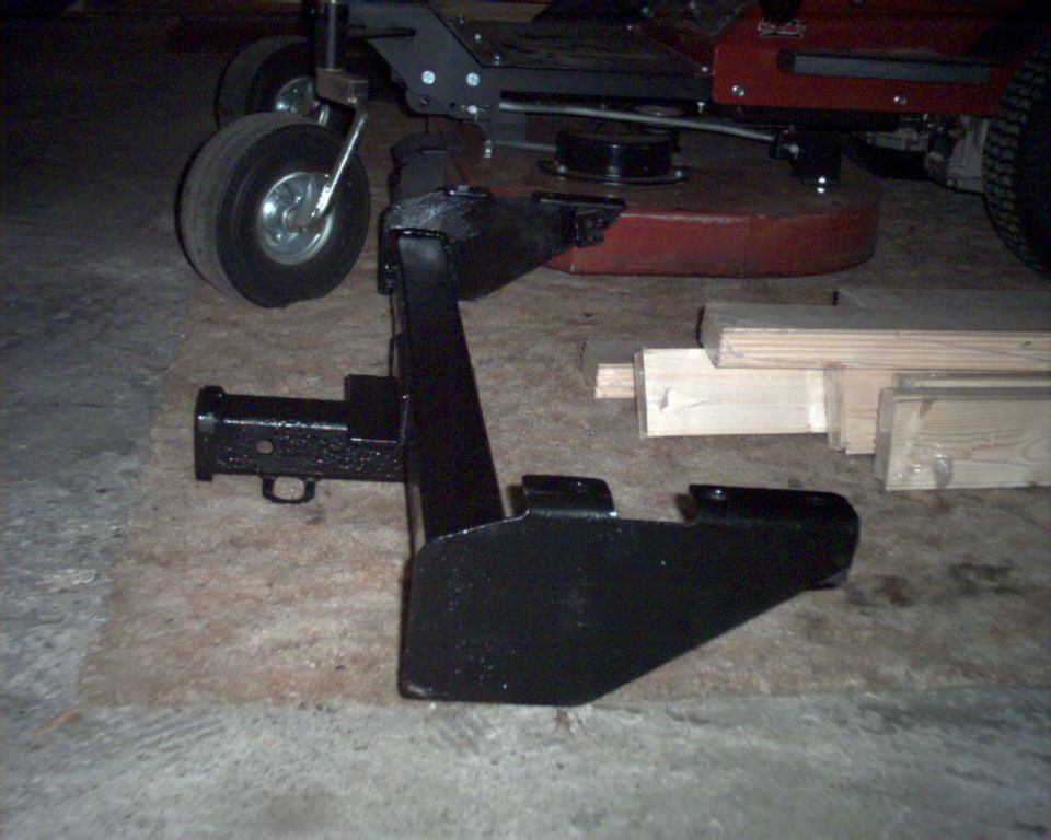Black steel hitch bracket on a floor in front of a red riding mower