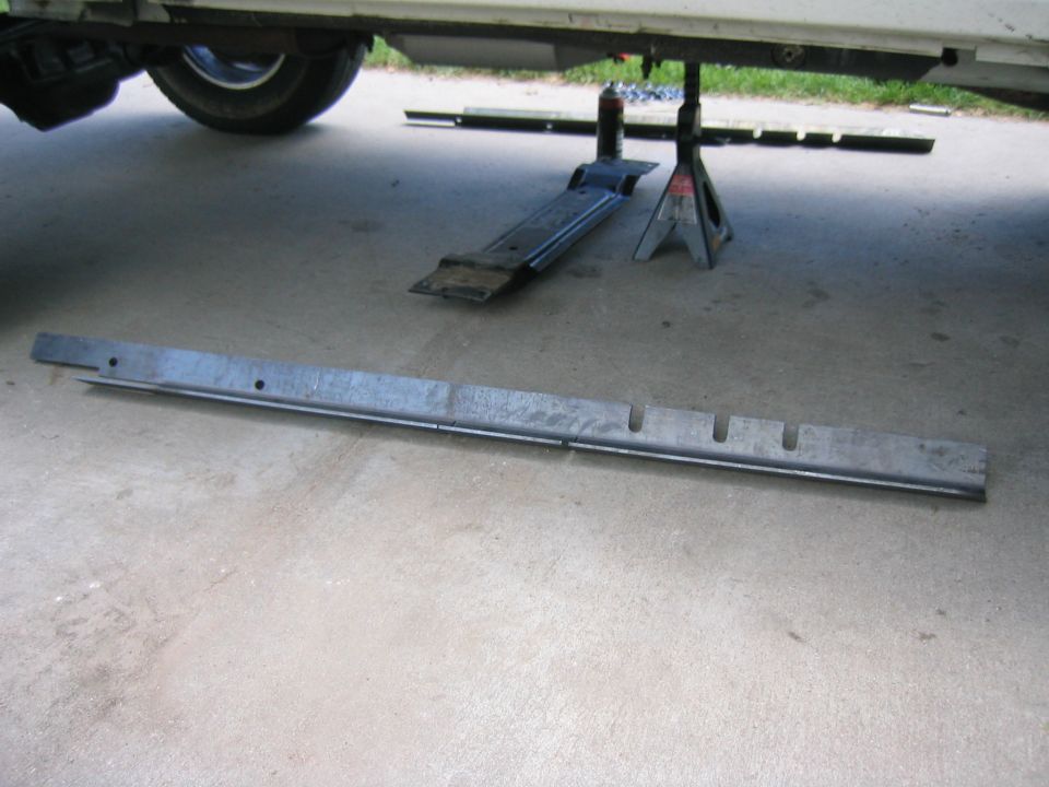 Long metal frame rail on concrete beside a vehicle on a jack stand