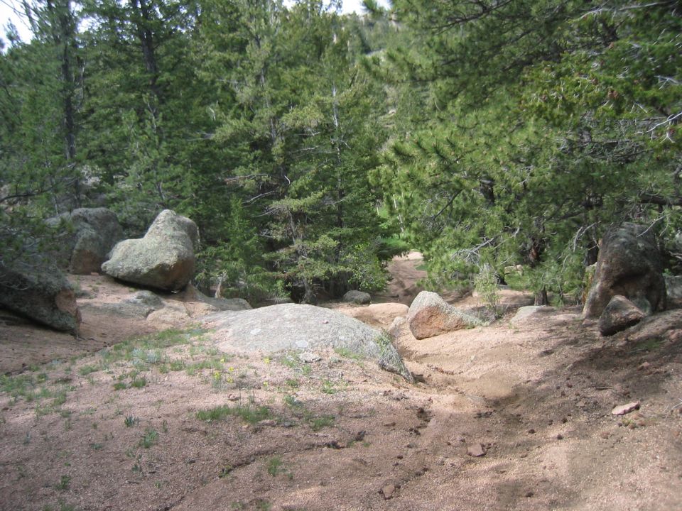 Sandy off-road trail squeezing between granite boulders in a pine forest