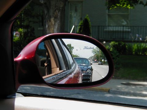 1997 Ford Taurus - Side mirror reflection shows a black car behind the red vehicle, with other cars visible on the road.