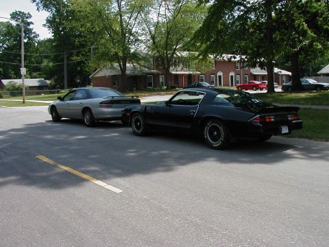1997 Ford Taurus - Two classic cars, a black Camaro Z28 and a silver sedan, are parked on a residential street.