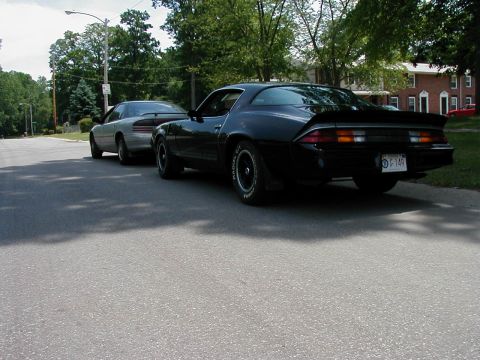 1997 Ford Taurus - A black 1970s Chevrolet Camaro is parked behind a silver sedan on a residential street.