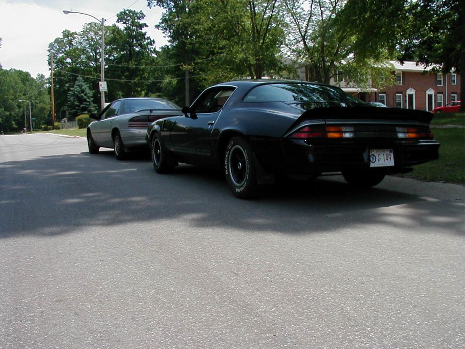 black 1970s Camaro and a silver sedan parked on a street