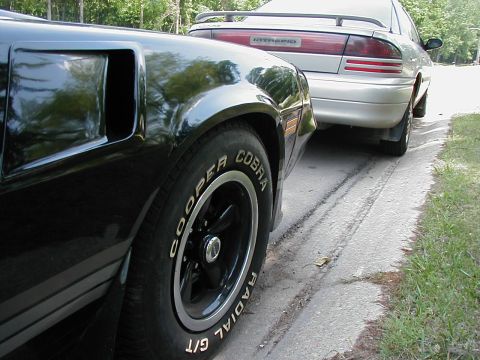 1997 Ford Taurus - A black car's rear quarter panel is in focus, with a silver Dodge Intrepid parked behind it on a roadside.