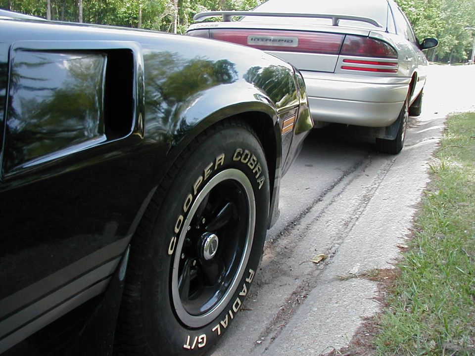 Black car's rear fender and tire, with a silver Intrepid car behind it
