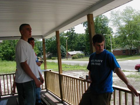 1997 Ford Taurus - Three young men stand on a covered porch, looking out at a residential street with trees and houses.