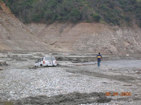 1985 Ford Bronco - A person walks away from a white SUV that is stuck in a muddy, rocky terrain.