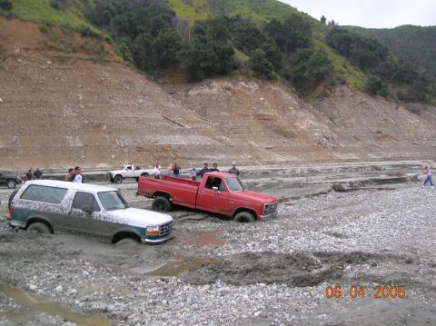 1985 Ford Bronco - A 1995 Ford Bronco is stuck in the mud alongside a red pickup truck in a dry riverbed.