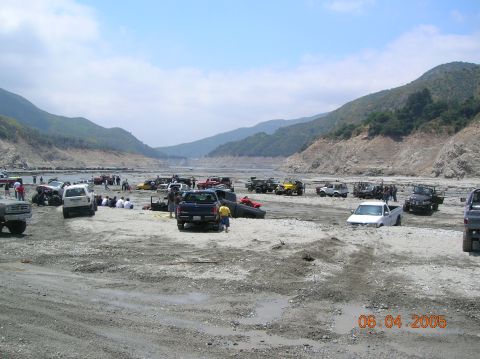 1985 Ford Bronco - Off-road enthusiasts gather in a dry riverbed with their vehicles on a sunny day.