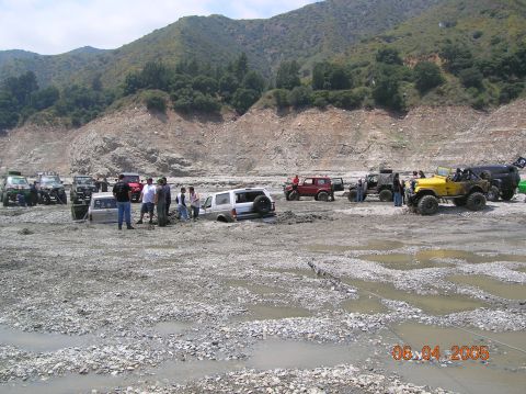 1985 Ford Bronco - Multiple off-road vehicles, including a 1985 Ford Bronco, are stuck in a muddy, rocky terrain.