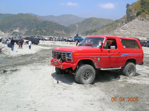 1985 Ford Bronco - Red Ford Bronco parked in a dry riverbed with mountains in the background.