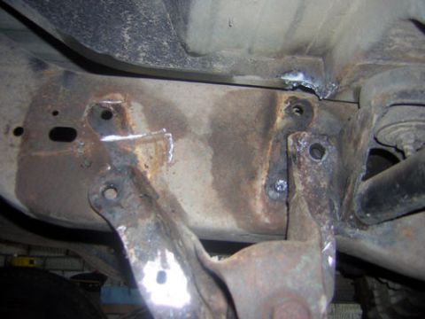 1995 Ford Bronco - Close-up view of a heavily rusted vehicle frame section showing recent welding repairs and attachment points.