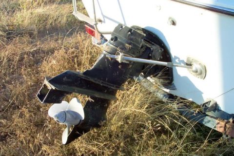 1990 Ford Bronco - Outboard motor and propeller of a boat resting on dry, grassy terrain.