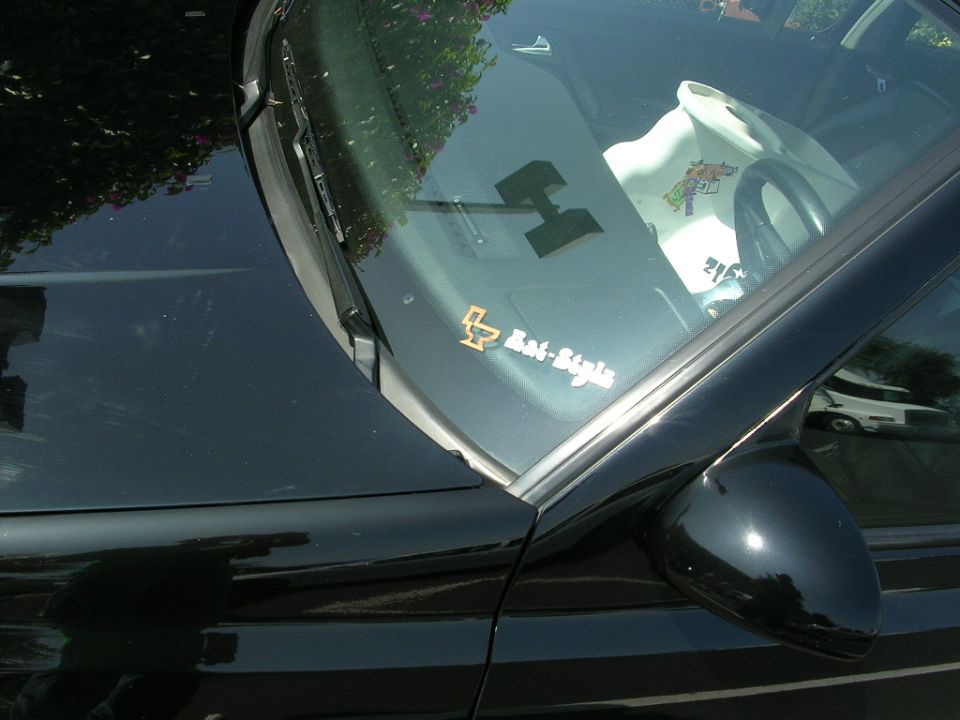 Car windshield with a large 'H' sticker and a 'Rat-Style' sticker. A white shirt with a cartoon character is on the passenger seat
