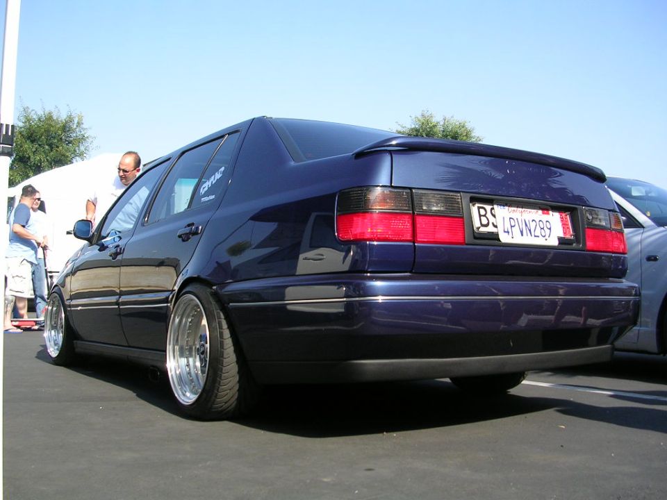 dark blue sedan with custom wheels and spoiler, parked next to another car