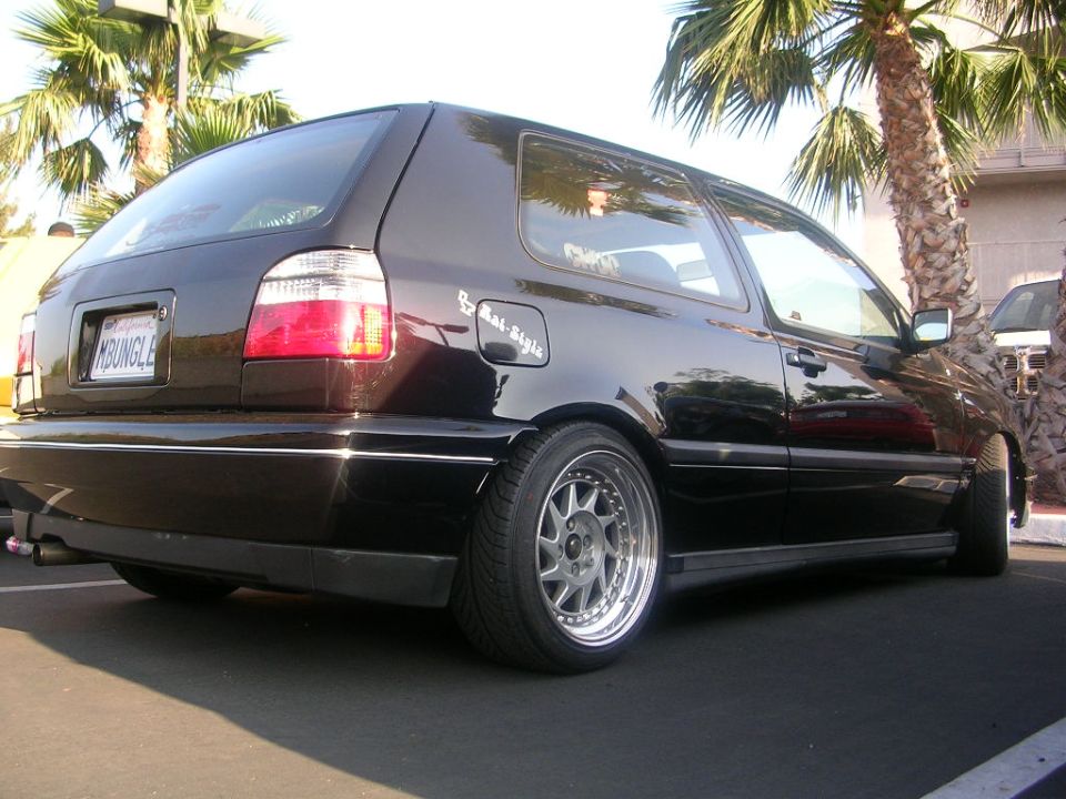 Black hatchback rear view with custom wheels and license plate reading 'MOUNGLE'