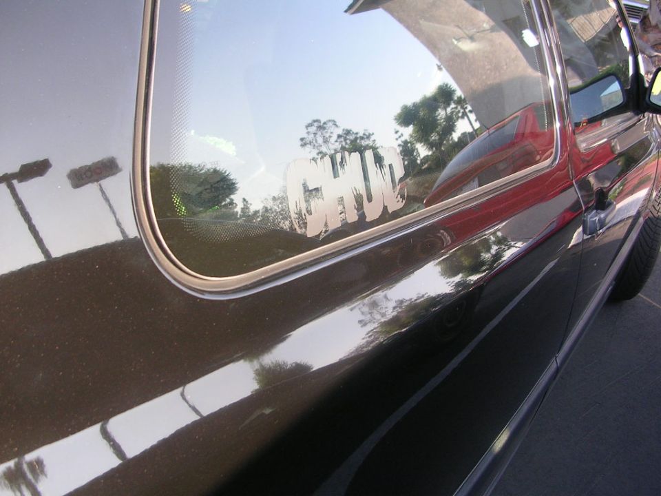 Close-up of a dark car's side door and rear window with a white "CHUD" sticker