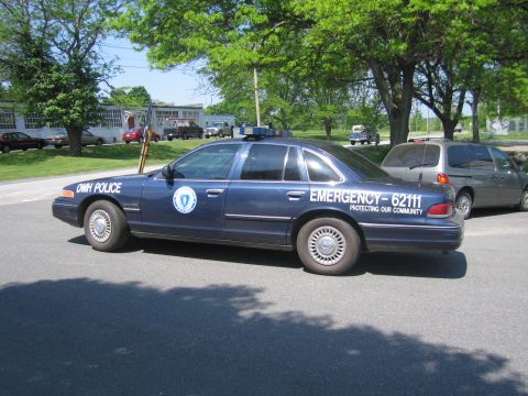 1991 Ford LTD Crown Victoria - A dark blue police car, possibly a Ford Crown Victoria, is parked with emergency markings visible on its side.
