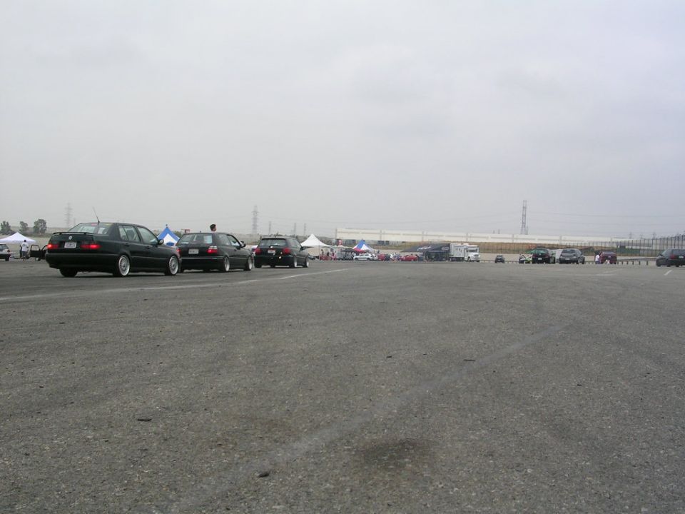 Several cars parked on asphalt under an overcast sky, with tents and trucks in the background
