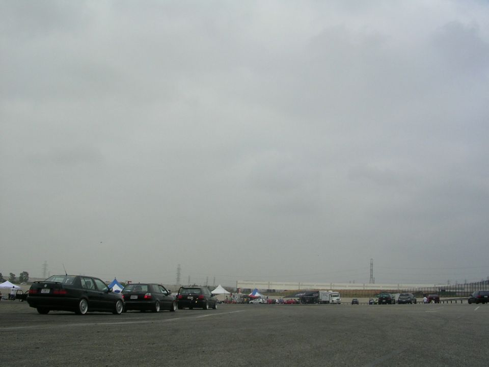 Several dark sedans and SUVs parked in an open lot under a cloudy sky