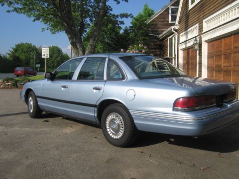 1991 Ford LTD Crown Victoria - A light blue sedan is parked in front of a wooden house with garage doors.