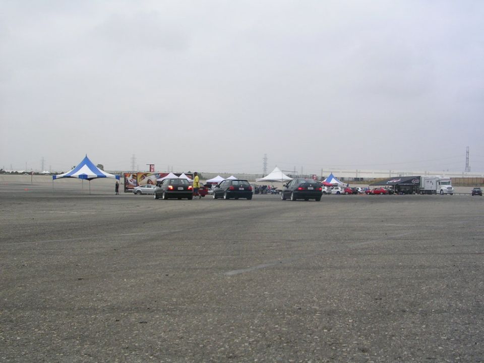 Several cars parked near tents at an outdoor event with a truck in the background
