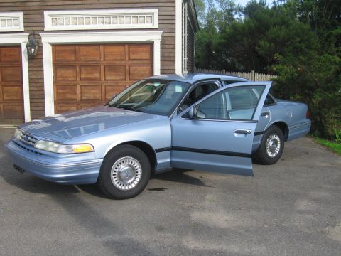 1991 Ford LTD Crown Victoria - A light blue sedan with its front doors ajar sits in a driveway.