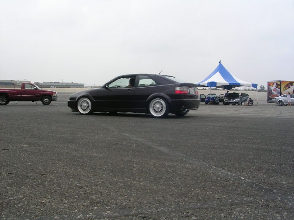 Black coupe with aftermarket wheels and a red pickup truck on asphalt