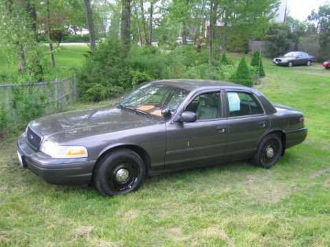 1991 Ford LTD Crown Victoria - This dark gray sedan is parked on a grassy lawn with trees in the background. A second vehicle is visible in the distance.