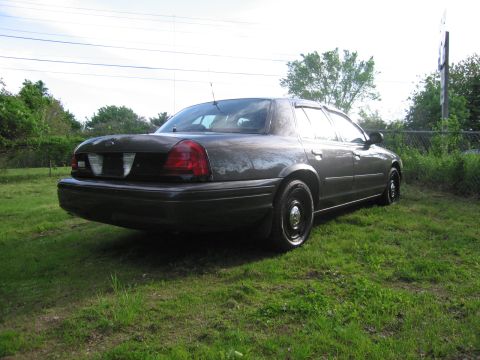 1991 Ford LTD Crown Victoria - Rear view of a dark sedan, possibly a Ford Crown Victoria, parked outdoors on a grassy area.