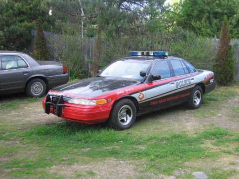 1991 Ford LTD Crown Victoria - A police car with "POLICE" markings and a light bar is parked next to another vehicle.