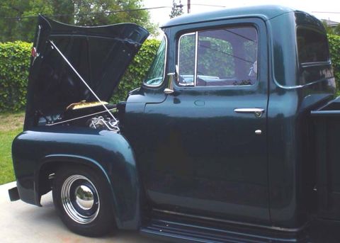 1956 Ford F-100 - A dark green 1956 Ford F-100 pickup truck is shown with its hood open, revealing the engine bay.