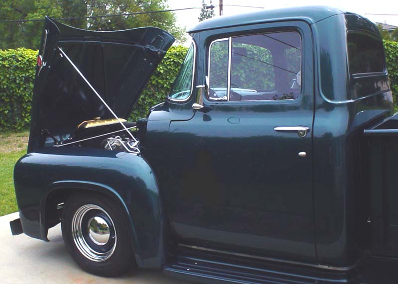 Dark green 1956 Ford F-100 pickup truck with hood open, chrome trim, and chrome hubcaps