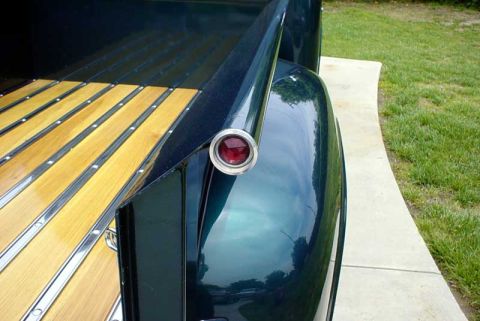 1956 Ford F-100 - Rear view of a dark green 1953 Ford F-100 truck, highlighting the wooden bed and a single round taillight.