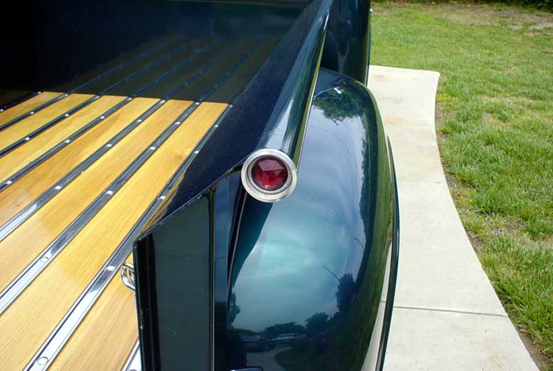 Dark green 1953 Ford F-100 truck bed with wood planks and chrome trim, close-up on round red taillight