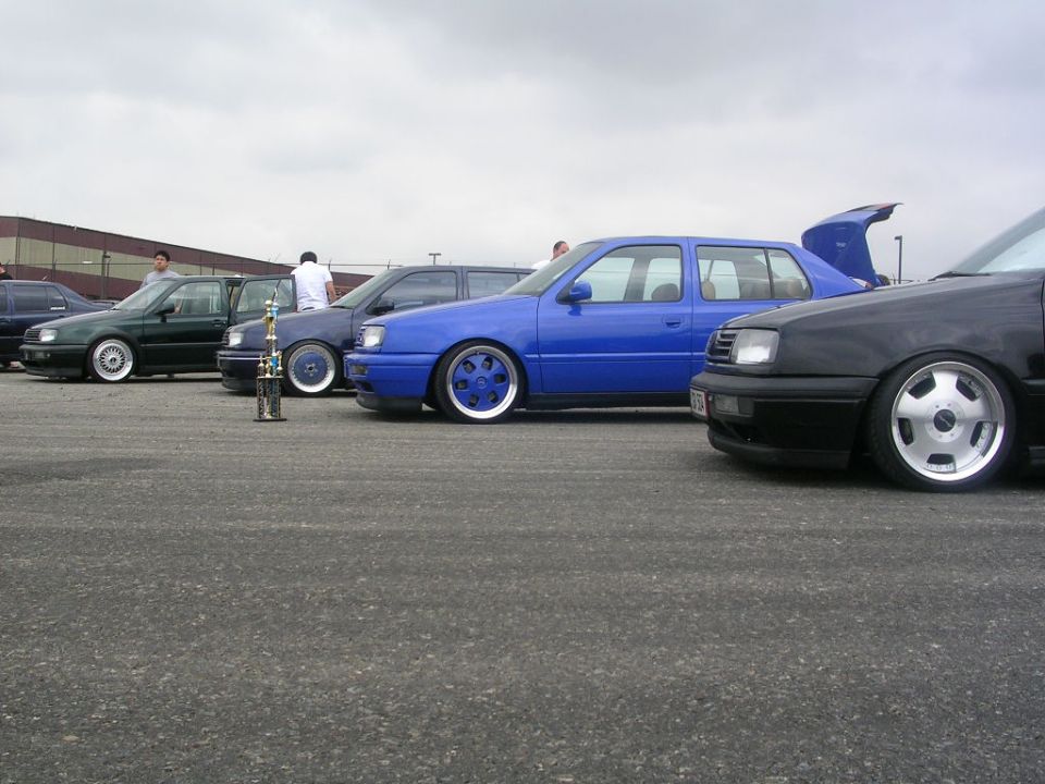 Line of modified sedans, blue car with custom wheels, trophy on pavement