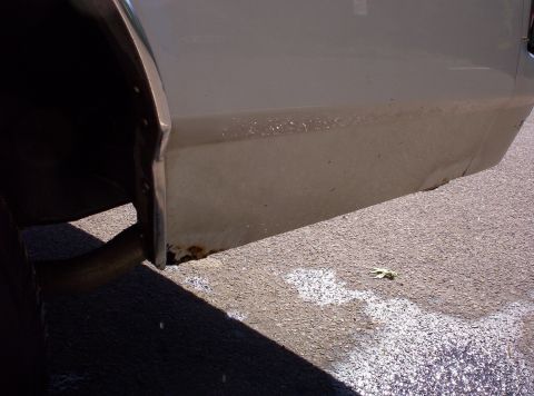 1991 Ford LTD Crown Victoria - The rear quarter panel of a tan 1991 Ford Crown Victoria LTD shows rust near the exhaust pipe.