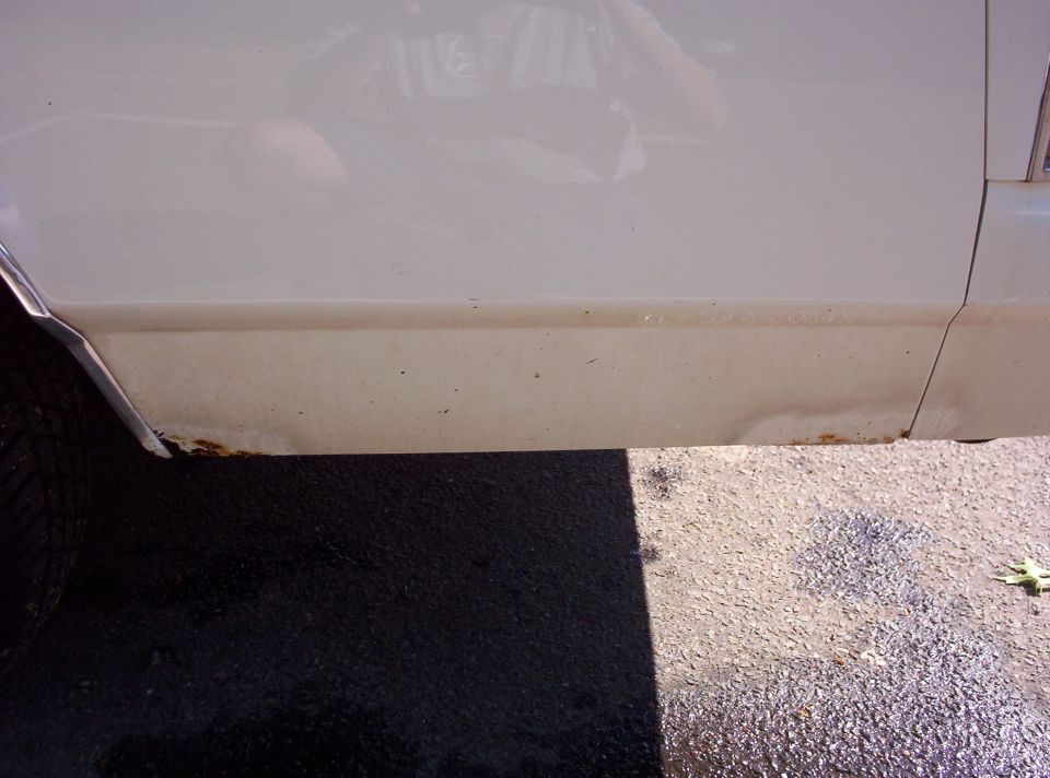 White car lower body panel showing rust and damage