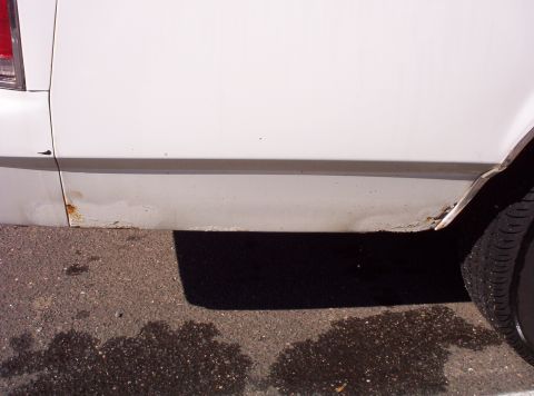 1991 Ford LTD Crown Victoria - Close-up of a white car's lower body panel showing rust and damage.