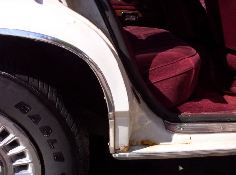 1991 Ford LTD Crown Victoria - Close-up of the rear passenger door area of a white 1991 Ford Crown Victoria LTD, revealing rust and a maroon velour seat.