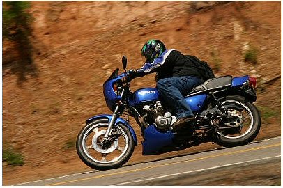 1985 Ford Crown Victoria LTD - A rider on a blue motorcycle navigates a turn on a scenic road.