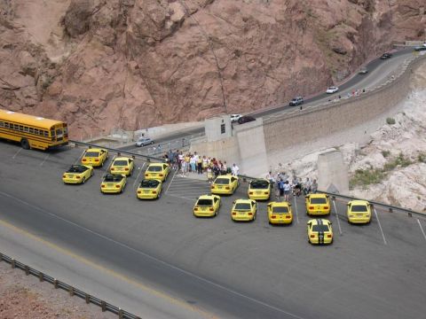 2002 Ford Mustang - A group of yellow cars are parked in a lot next to a large dam, with a school bus also present.