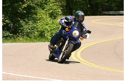 1985 Ford Crown Victoria LTD - A motorcyclist navigates a curve on a scenic road, demonstrating skillful riding.