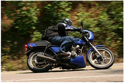 1985 Ford Crown Victoria LTD - Motorcycle rider on a blue bike cruises down a tree-lined road.