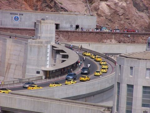 2002 Ford Mustang - A convoy of yellow Ford Mustangs drives along a road with Hoover Dam in the background.