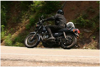 1985 Ford Crown Victoria LTD - Motorcyclist navigates a winding road surrounded by lush greenery.