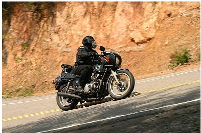 1985 Ford Crown Victoria LTD - A motorcycle rider navigates a curve on a paved road with a rocky embankment.